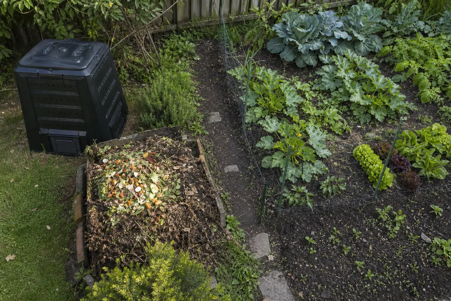 Overhead view of a backyard with separate compost bin and open pile setups side by side